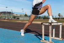 Primo piano di una giovane donna forte in abbigliamento sportivo che si estende sullo sgabello durante l'allenamento allo stadio — Foto stock