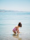Vista lateral de adorable niña en traje de baño de pie en agua tibia de mar tranquilo - foto de stock