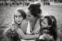Frau mit verspielten Töchtern, die am Sandstrand liegen und zusammen Spaß haben, Schwarz-Weiß-Foto — Stockfoto
