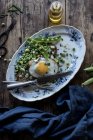 Served plate with sauteed green peas and fried egg on wooden table — Stock Photo