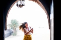 Donna felice utilizzando il telefono cellulare vicino paesaggio desertico in piedi sul balcone di pietra, Marocco — Foto stock