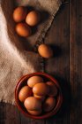 Chicken eggs with bowl and sackcloth on wooden table — Stock Photo