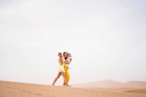 Alegre elegante duas mulheres loiras amigas usando telefone celular enquanto caminhava no deserto de Marrocos — Fotografia de Stock