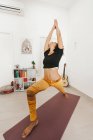 Attrayant jeune femme effectuant posture de yoga avec les bras croisés étirés sur le tapis dans la salle de lumière — Photo de stock