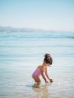 Вид збоку чарівна дівчинка-малюк у купальнику, що стоїть у теплій воді спокійного моря — стокове фото