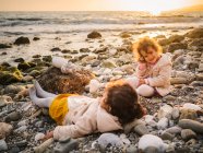 Toddler female twins playing on stony seashore on background of calm water — Stock Photo
