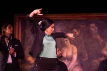 Donna in costume nero danza flamenco vicino a musicisti ispanici di sesso maschile durante la performance contro la pittura sul palco scuro — Foto stock