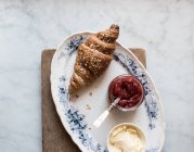 Teller mit knusprigem Croissant und Butter und Erdbeermarmelade auf Holzbrett serviert — Stockfoto
