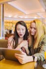 Junge kaukasische Frau zeigt einem erstaunten asiatischen Freund ein Video auf dem Tablet, während sie zusammen am Cafétisch sitzt — Stockfoto