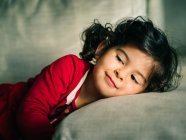 Adorable female kid in red dress smiling while resting on pillow at home — Stock Photo