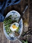 Plato servido con guisantes verdes salteados y huevo frito en mesa de madera - foto de stock