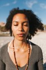 Primer plano de la joven atractiva afroamericana meditando en la playa - foto de stock