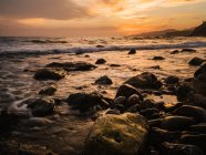 Vista pitoresca de pedras molhadas à beira-mar calma contra o céu do pôr-do-sol — Fotografia de Stock