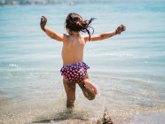 Visão traseira da menina bonito alegre anônimo jogando na água do mar no fundo da costa calma — Fotografia de Stock