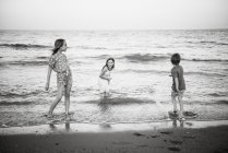 Groupe de petits garçons avec deux sœurs jouant dans une vague d'eau peu profonde sur la côte, photo en noir et blanc — Photo de stock
