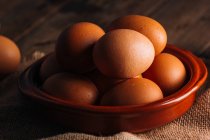 Chicken eggs in bowl on wooden table — Stock Photo
