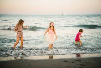 Grupo de niños pequeños con dos hermanas jugando en una ola de agua poco profunda en la costa - foto de stock