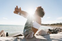 Молодая афроамериканка в позе йоги на фоне спокойной воды в солнечный день — стоковое фото
