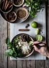 Человеческая рука с палочками для еды и суп из Фо с лапшой на мраморной доске на деревянном столе со специями — стоковое фото