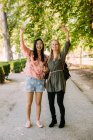 Excited multiracial females pointing and waving hands while standing on park alley on sunny day — Stock Photo