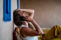 Felice donna bionda seduta sul divano in terrazza in stile orientale e utilizzando un telefono cellulare in Marocco — Foto stock