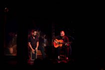 Homens hispânicos tocando percussão e guitarra acústica durante a performance do flamenco no palco escuro — Fotografia de Stock