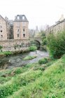 Paisaje de antiguos edificios de mampostería con río poco profundo que fluye entre arbustos verdes, Escocia - foto de stock