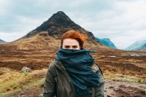 Beautiful ginger woman swaddled in scarf standing against picturesque mountains of Scotland — Stock Photo