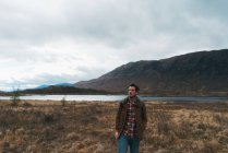 Erwachsener Mann mit Rucksack steht in malerischem abgelegenen Tal, Berge und See schauen weg — Stockfoto
