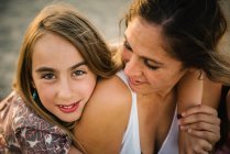 Mulher adulta abraçando com amor uma menina bonita na praia de areia ao pôr do sol luz — Fotografia de Stock