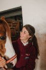 Teenagermädchen umarmt mit kleinem Pony in niedlichem Hut auf Ohren im Stall stehend — Stockfoto
