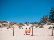 Rückansicht von kleinen Schwestern in leuchtend orangefarbenen Kleidern, die an sonnigen Tagen gemeinsam am Meer spazieren — Stockfoto