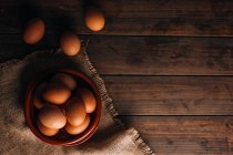 Huevos de pollo con tazón y saco sobre mesa de madera - foto de stock