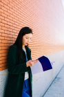 Азиатка читает учебник, опираясь на кирпичную стену в университетском городке — стоковое фото