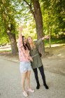 Возбужденные многорасовые женщины, указывающие и машущие рукой, стоя на аллее парка в солнечный день — стоковое фото