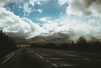 Malerischer Blick auf Berg und leere Autobahn im Wüstengebiet gegen wolkenverhangenen Himmel — Stockfoto