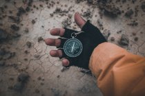 Closeup of hand in black fingerless glove holding compass on desert place — Stock Photo
