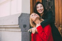 Mulher asiática feliz sorrindo e de pé contra a porta ornamental de edifício envelhecido e abraçando amigo caucasiano — Fotografia de Stock