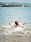 Vue arrière de fille mignonne joyeuse anonyme jouant dans l'eau de mer sur fond de bord de mer calme — Photo de stock