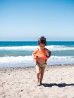 Сзади вид маленьких сестричек в ярко-оранжевых платьях, идущих вместе по морю в солнечный день — стоковое фото
