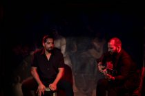 Hommes hispaniques jouant de la percussion et de la guitare acoustique lors d'un spectacle de flamenco sur scène sombre — Photo de stock