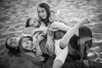 Черно-белое изображение женщины с веселыми дочерьми и сыном, лежащими на песчаном пляже и веселящимися вместе — стоковое фото