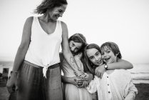 Black and white of adult laughing woman with adorable daughters and son embracing on beach — Stock Photo
