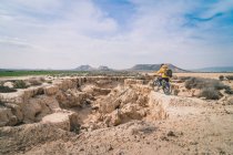 Homme avec vélo debout sur la pierre dans les collines du désert — Photo de stock