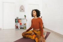Afro-americano giovane donna che esegue posa yoga con le gambe incrociate e meditando con gli occhi chiusi a casa — Foto stock