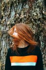 Bella giovane donna in felpa casual agitando con i capelli color zenzero contro il vecchio albero, Scozia — Foto stock