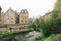 Paesaggio di vecchi edifici in muratura con fiume poco profondo che scorre tra cespugli verdi, Scozia — Foto stock