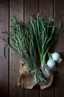 From above of bundle of green asparagus and fresh onion bulbs with green stems on wooden table — Stock Photo