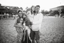 Дорослий люблячий чоловік і жінка з сином і дочками, що стоять разом на пляжі в спині, освітленій посмішкою на камеру, чорно-білому фото — стокове фото