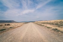 Wüste staubige Straße zwischen verlassenem Trockengebiet mit Vegetation in Halbwüste — Stockfoto